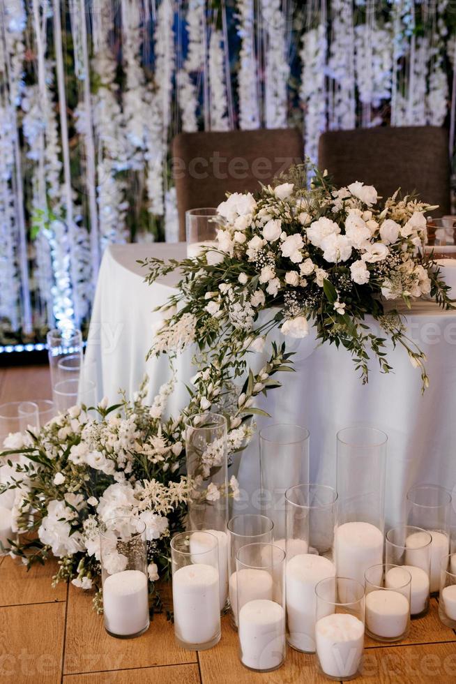 le présidium des jeunes mariés dans la salle de banquet du restaurant est décoré de bougies et de plantes vertes photo