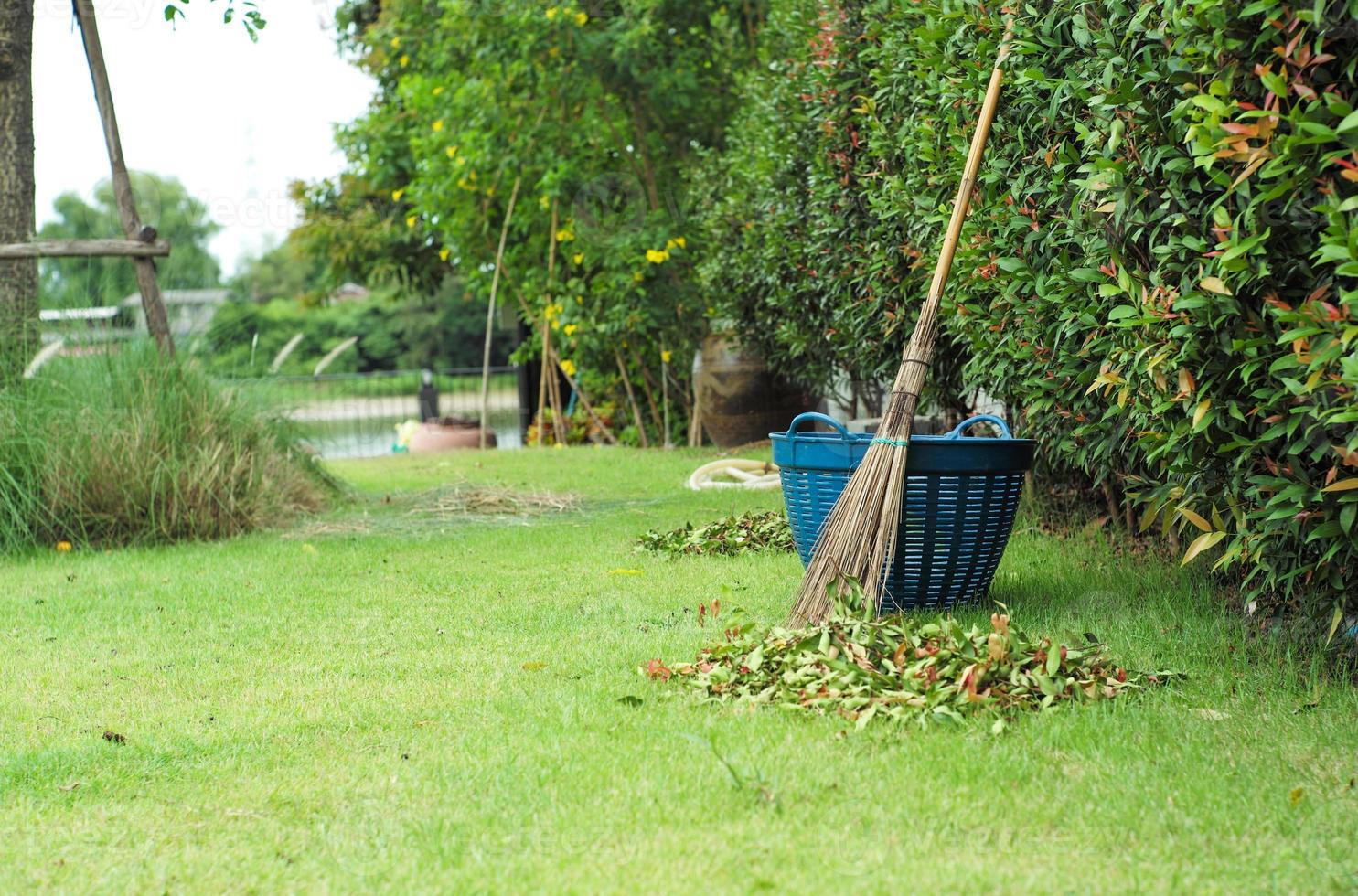 mise au point sélective sur le balai à feuilles de coco et le panier avec un tas flou de feuilles séchées au premier plan photo