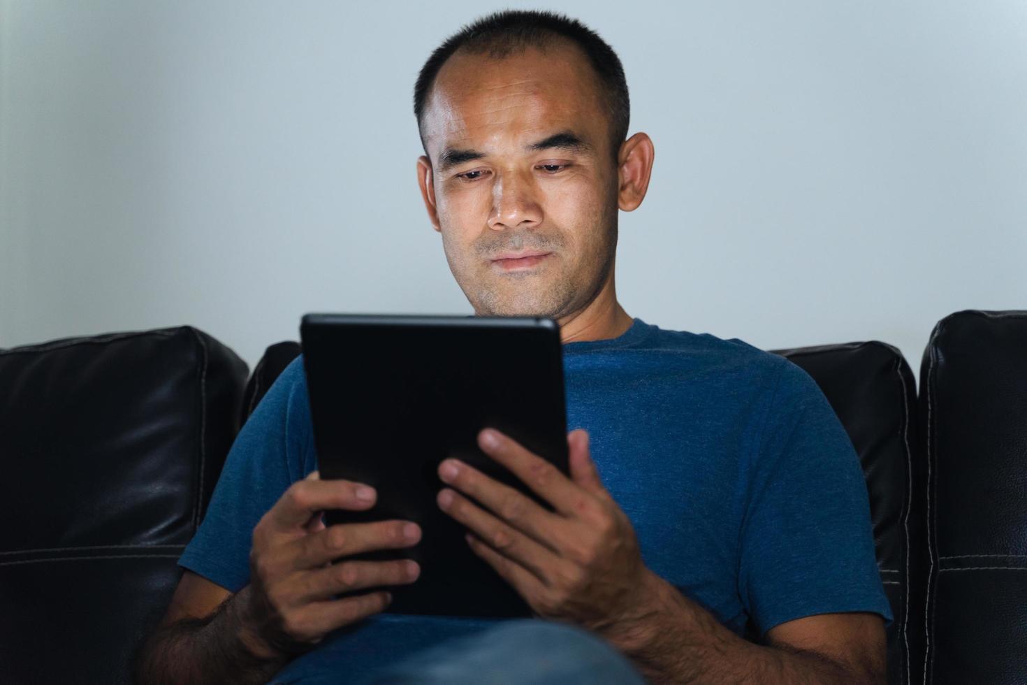 homme assis sur un canapé, utilisant une tablette pour travailler ou se détendre à la maison. travail à domicile concept. photo
