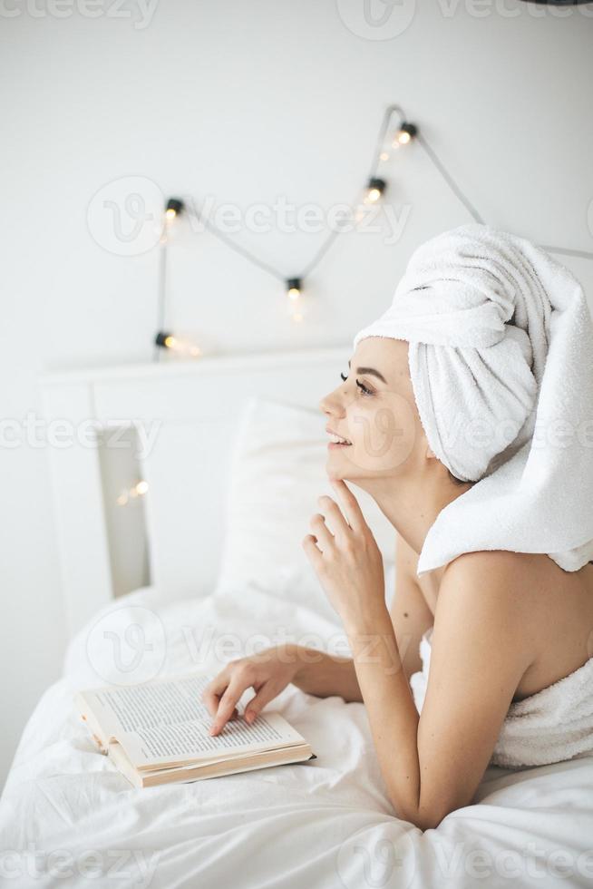 jeune femme heureuse lisant un livre papier au lit. photo