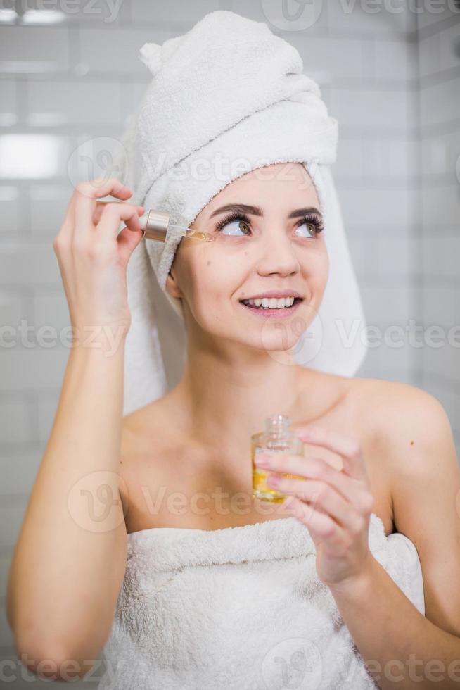 jeune femme en serviette blanche applique de l'huile hydratante sur la peau du visage. photo