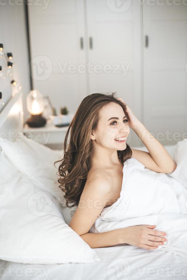 belle jeune femme se réveillant dans un lit confortable sur des draps frais blancs. photo