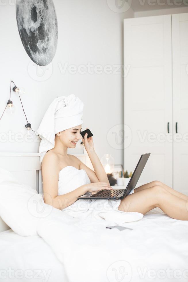 jeune femme travaillant dans un lit blanc à l'aide d'un ordinateur portable. photo