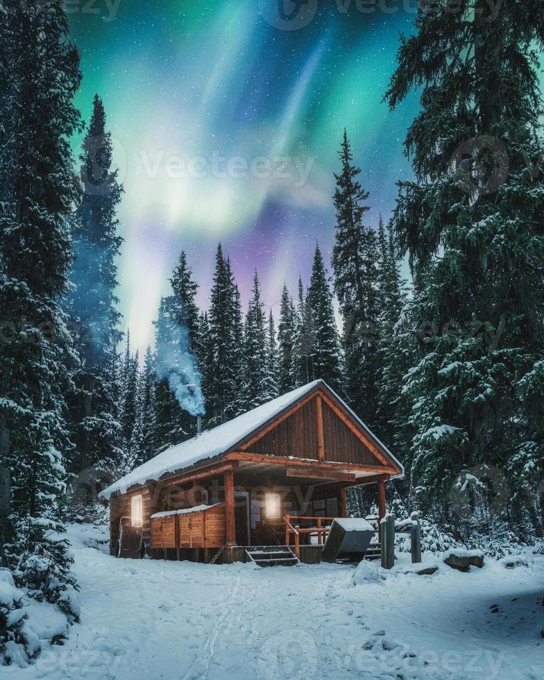 aurores boréales sur chalet en bois avec de la fumée sur la neige dans la forêt de pins au parc national yoho photo