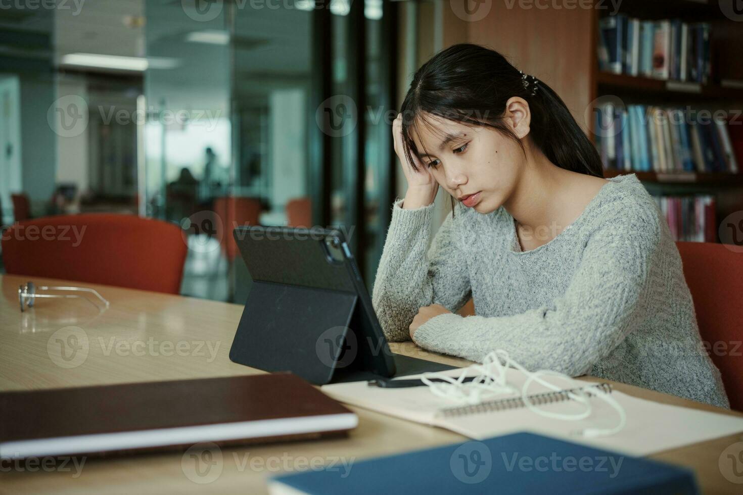 asiatique étudiant femme lis livres dans bibliothèque à université. Jeune fille stress fatigué avoir problème tandis que étude dur. tristesse concept photo