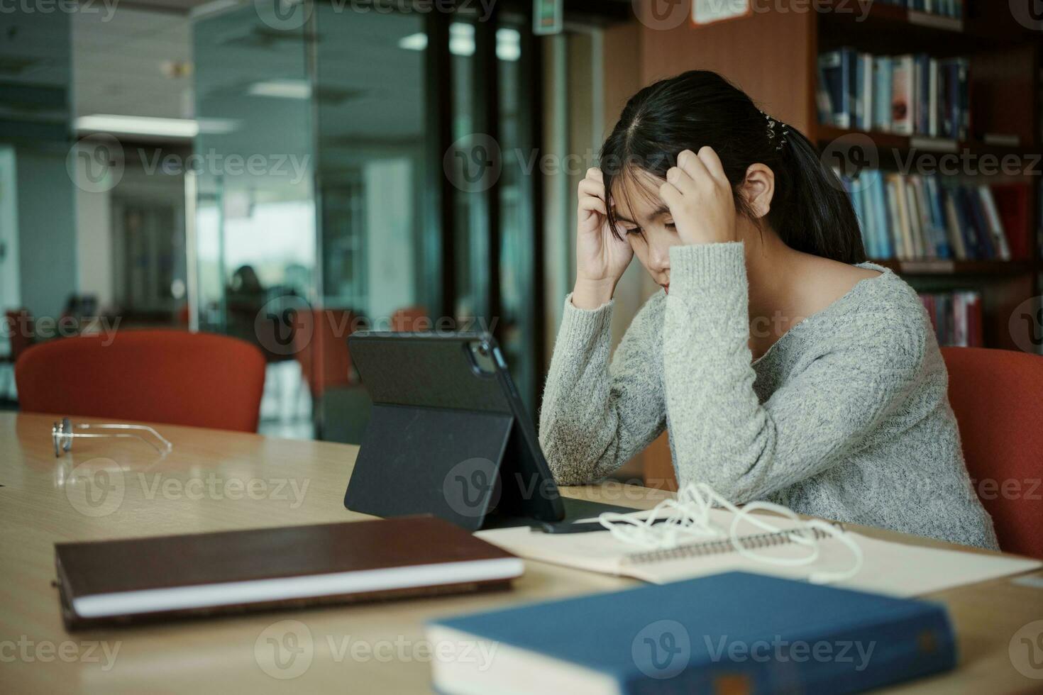 asiatique étudiant femme lis livres dans bibliothèque à université. Jeune fille stress fatigué avoir problème tandis que étude dur. tristesse concept photo