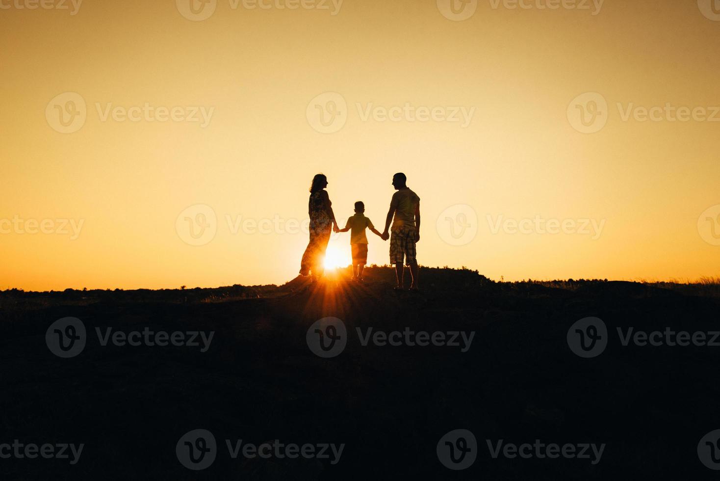 silhouettes d'une jeune famille heureuse heureuse contre un coucher de soleil orange photo