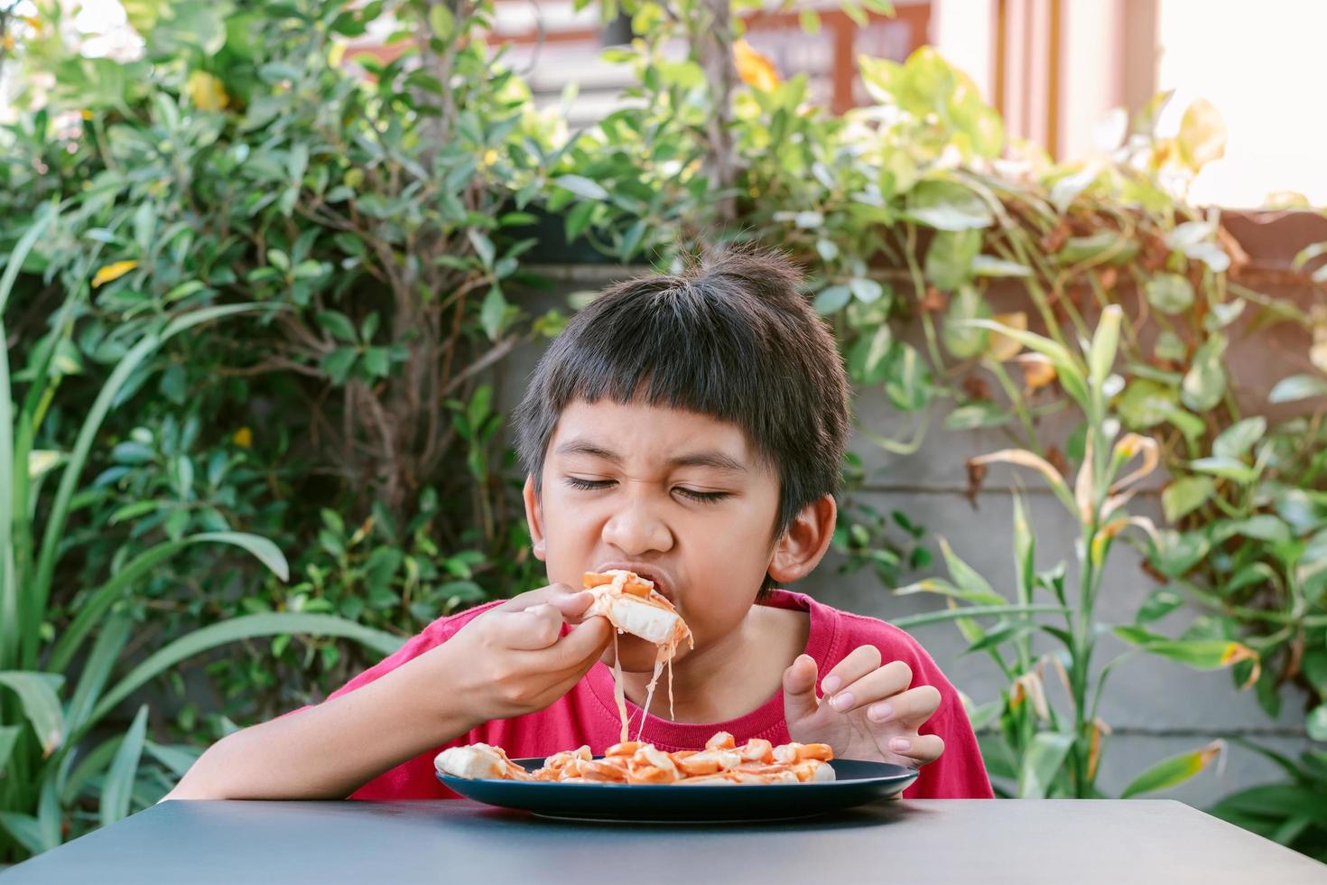 garçon mignon asiatique en chemise rouge mangeant de la pizza photo