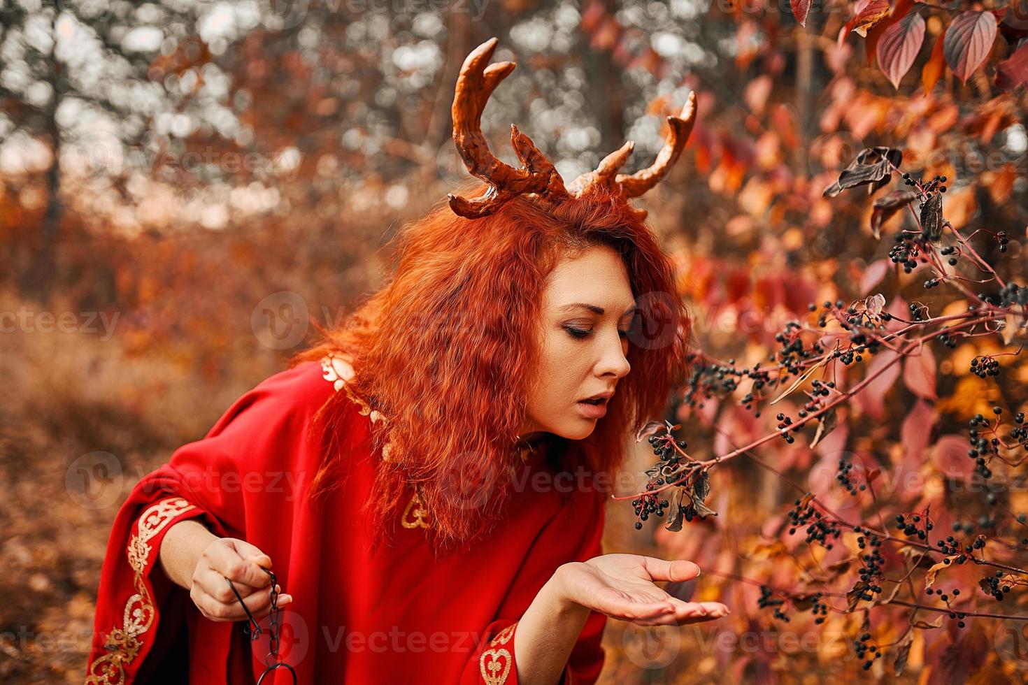 femme en longue robe rouge avec des cornes de cerf dans la forêt d'automne. photo