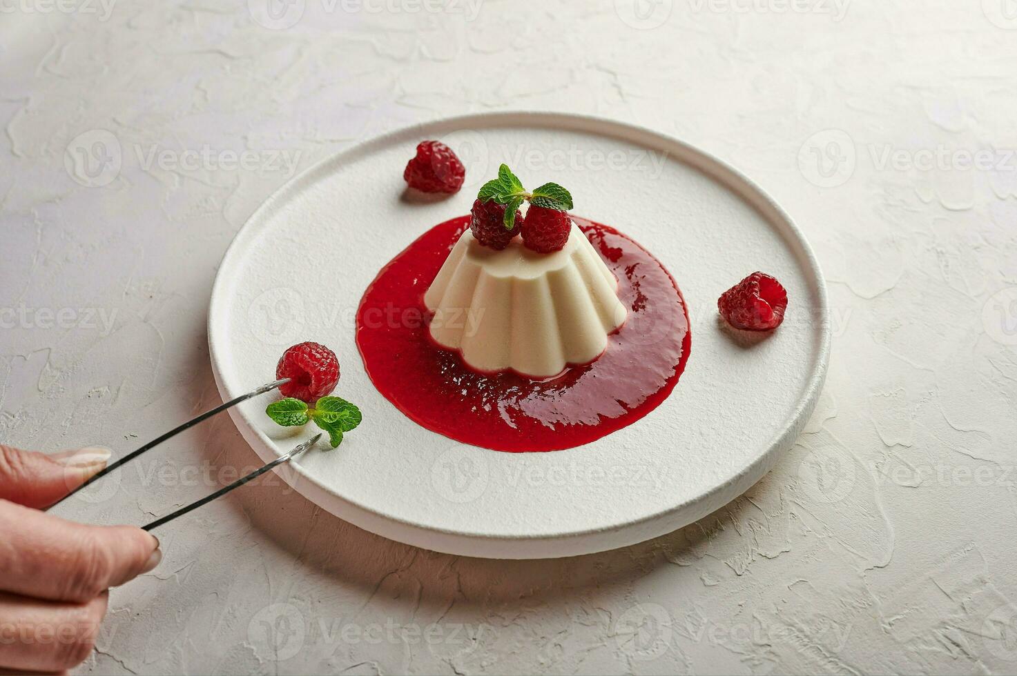 femme main met pince à épiler feuille menthe à panna cotta avec sirop, framboises et menthe photo