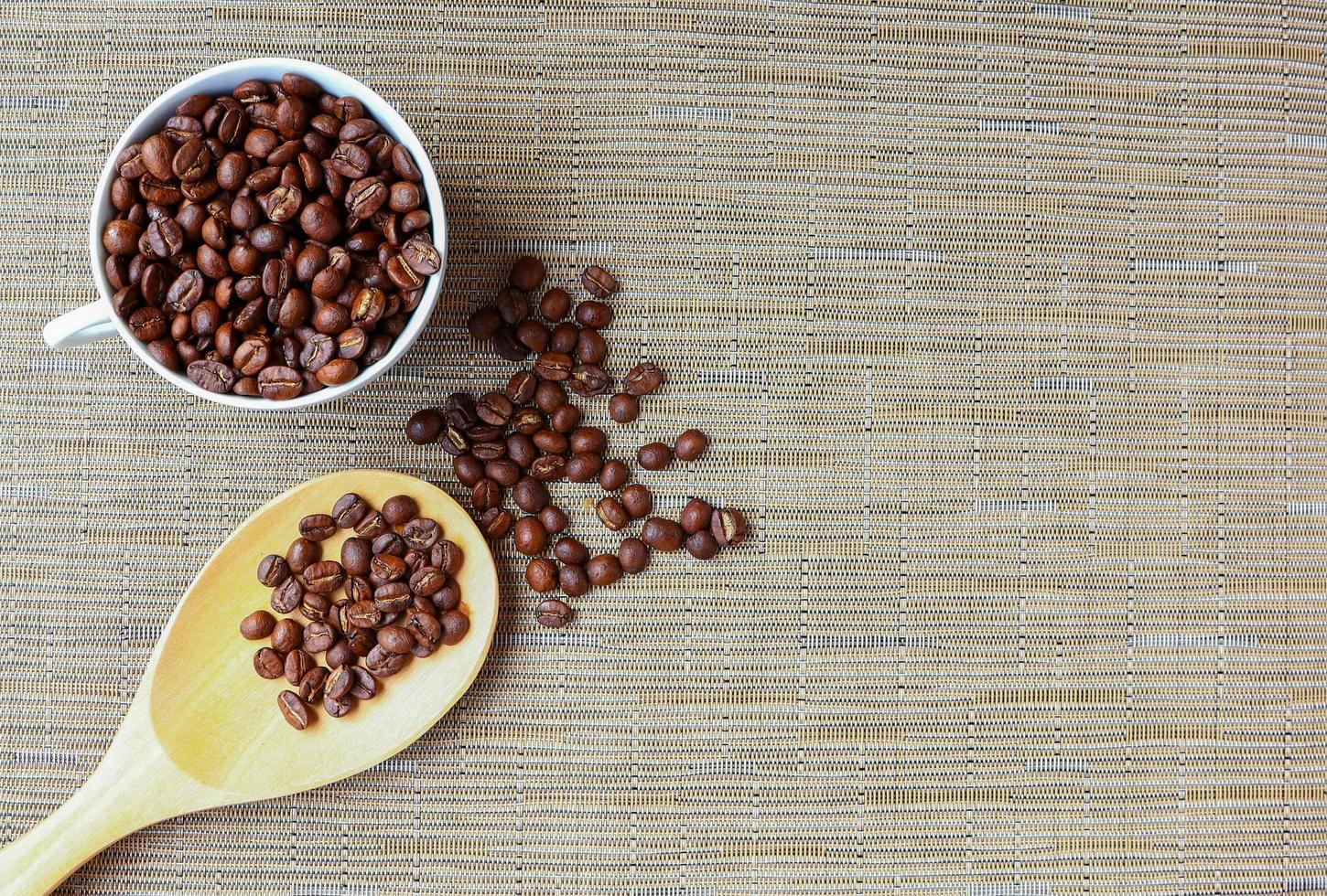 grains de café torréfiés dans une tasse blanche avec une cuillère en bois photo