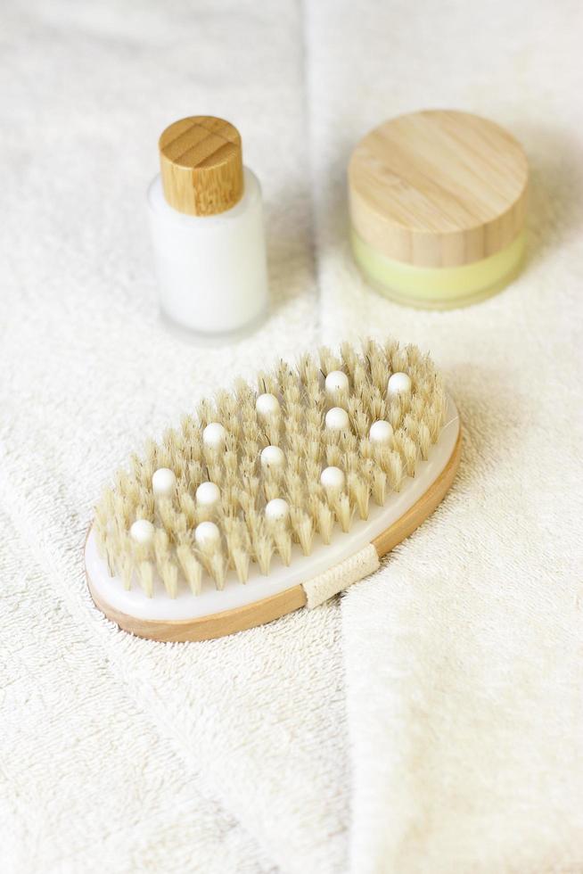 brosse naturelle en bois pour massage de la peau sèche sur une serviette blanche avec des bouteilles en cristal cosmétiques avec dessus en bambou en bois photo