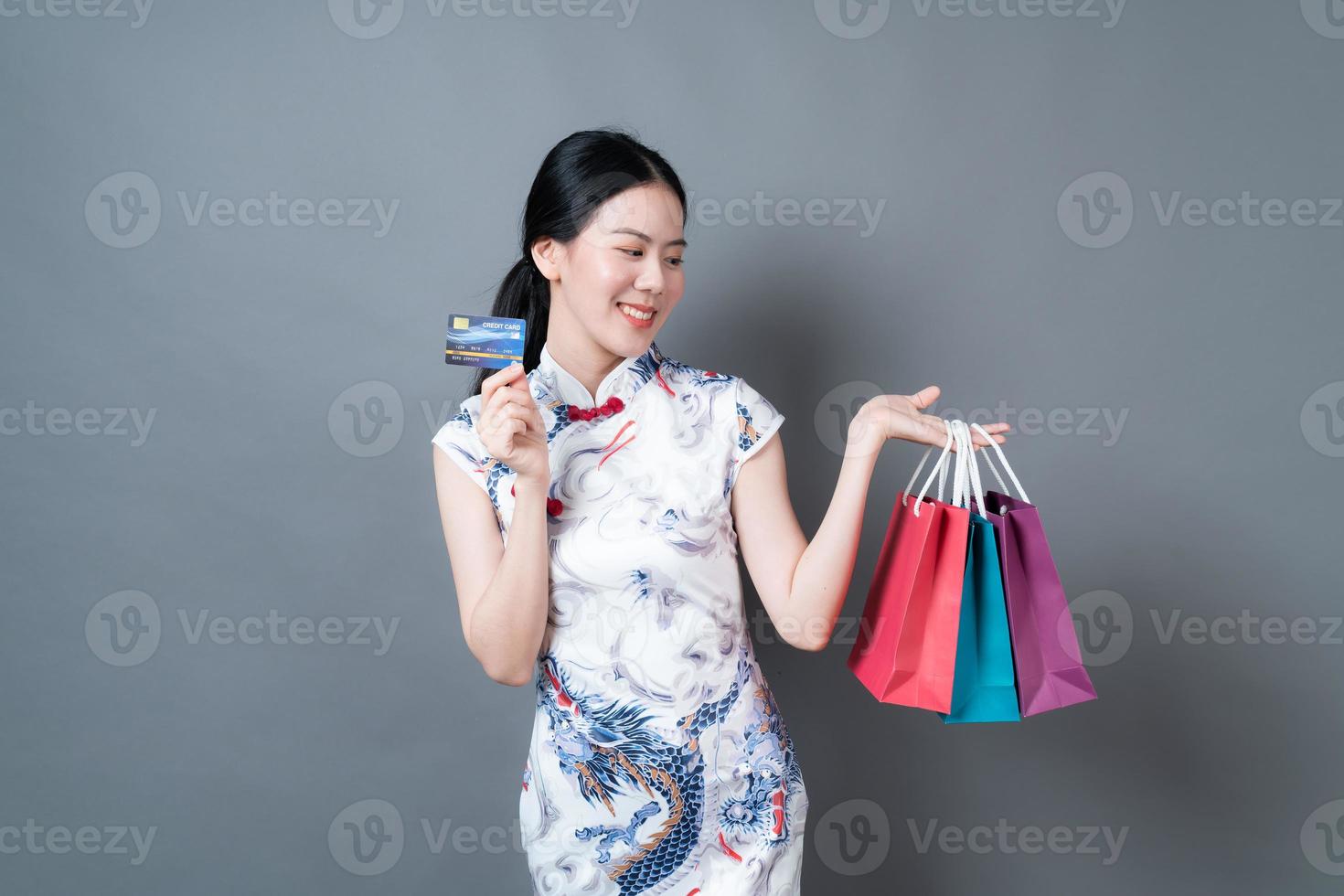 une femme asiatique porte une robe traditionnelle chinoise avec un sac à provisions et une carte de crédit photo