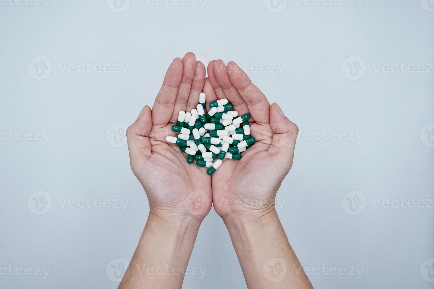 mains tenant beaucoup de capsules blanches et vertes sur fond gris photo
