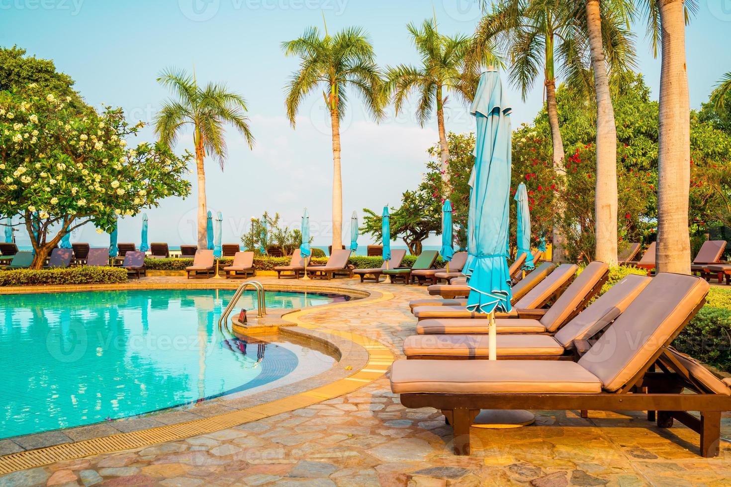 Chaises piscines et parasols autour de la piscine avec cocotiers - vacances et concept de vacances photo