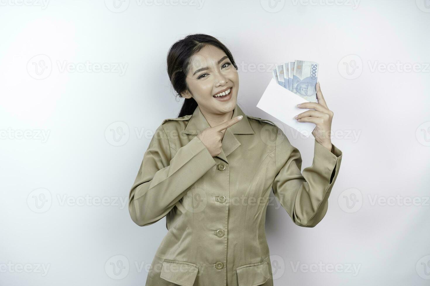 une souriant Jeune gouvernement ouvrier femme est portant kaki uniforme en portant en espèces argent dans indonésien Rupiah isolé par blanc Contexte photo