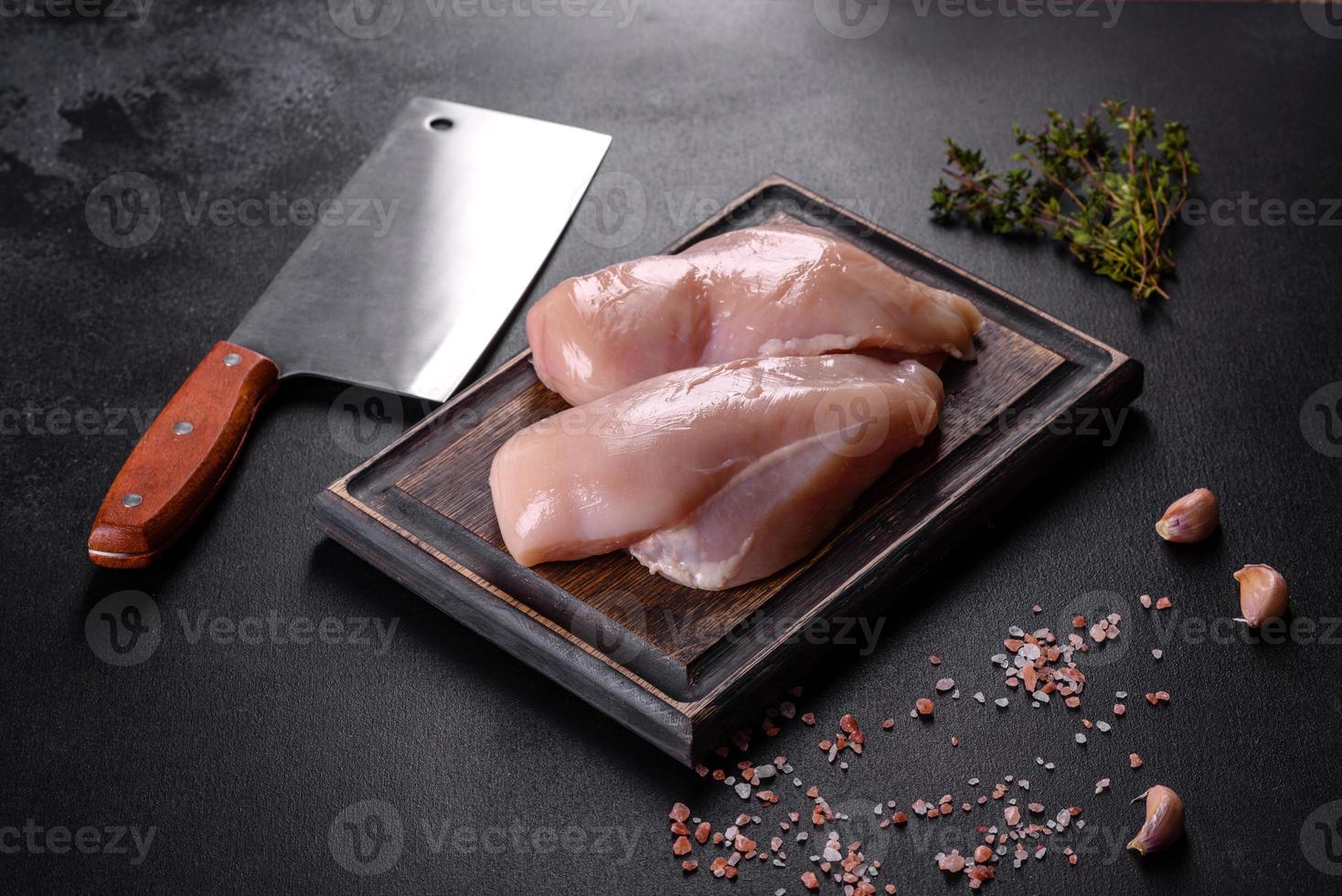 filet de poulet frais sur une table en béton foncé avec des épices et des herbes photo