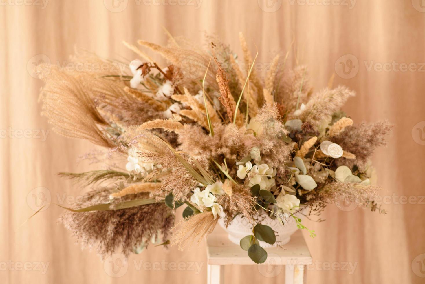 décorations de belles fleurs sèches dans un vase blanc sur fond de tissu beige photo