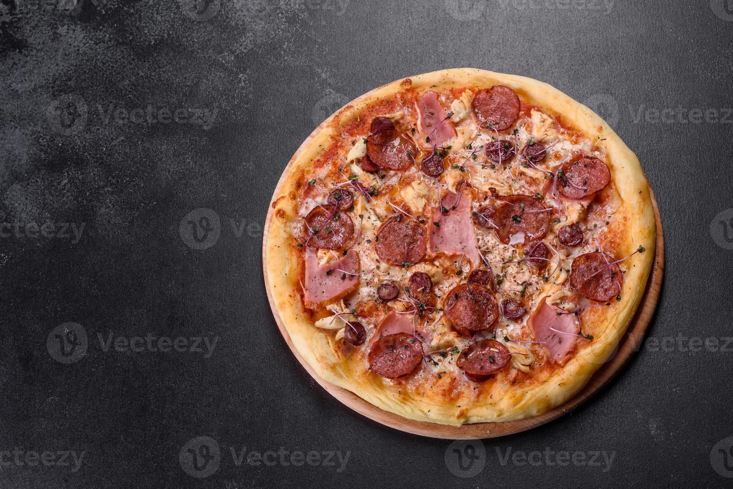 délicieuse pizza fraîche au four avec tomates, salami et bacon sur fond de béton foncé photo