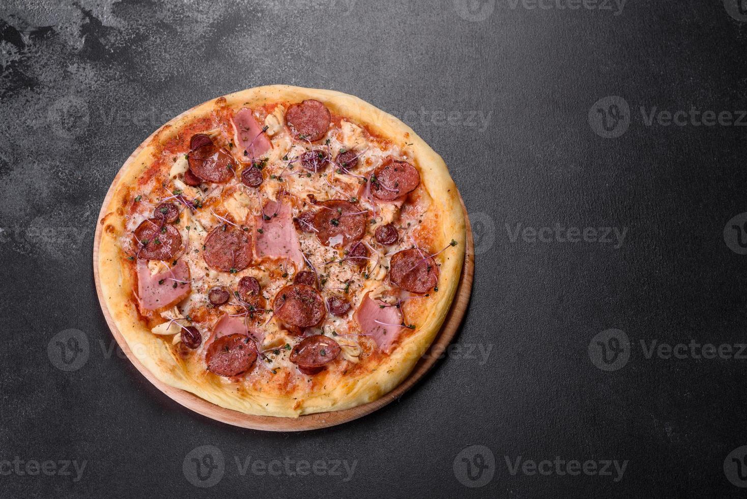 délicieuse pizza fraîche au four avec tomates, salami et bacon sur fond de béton foncé photo