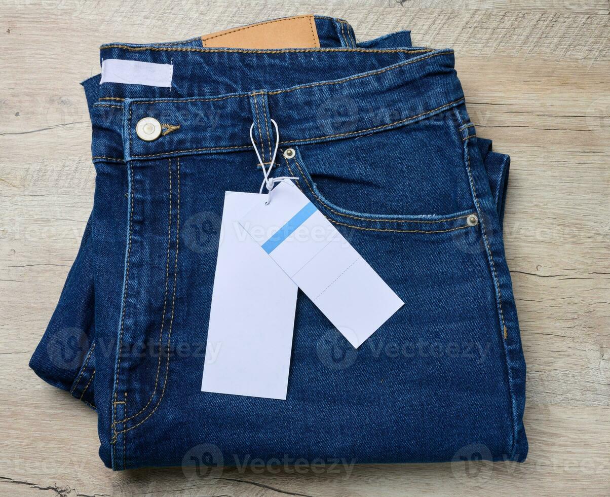 bleu jeans sur une en bois surface. le un pantalon sont soigneusement plié, et là est une marron cuir pièce à le taille de le jeans. photo