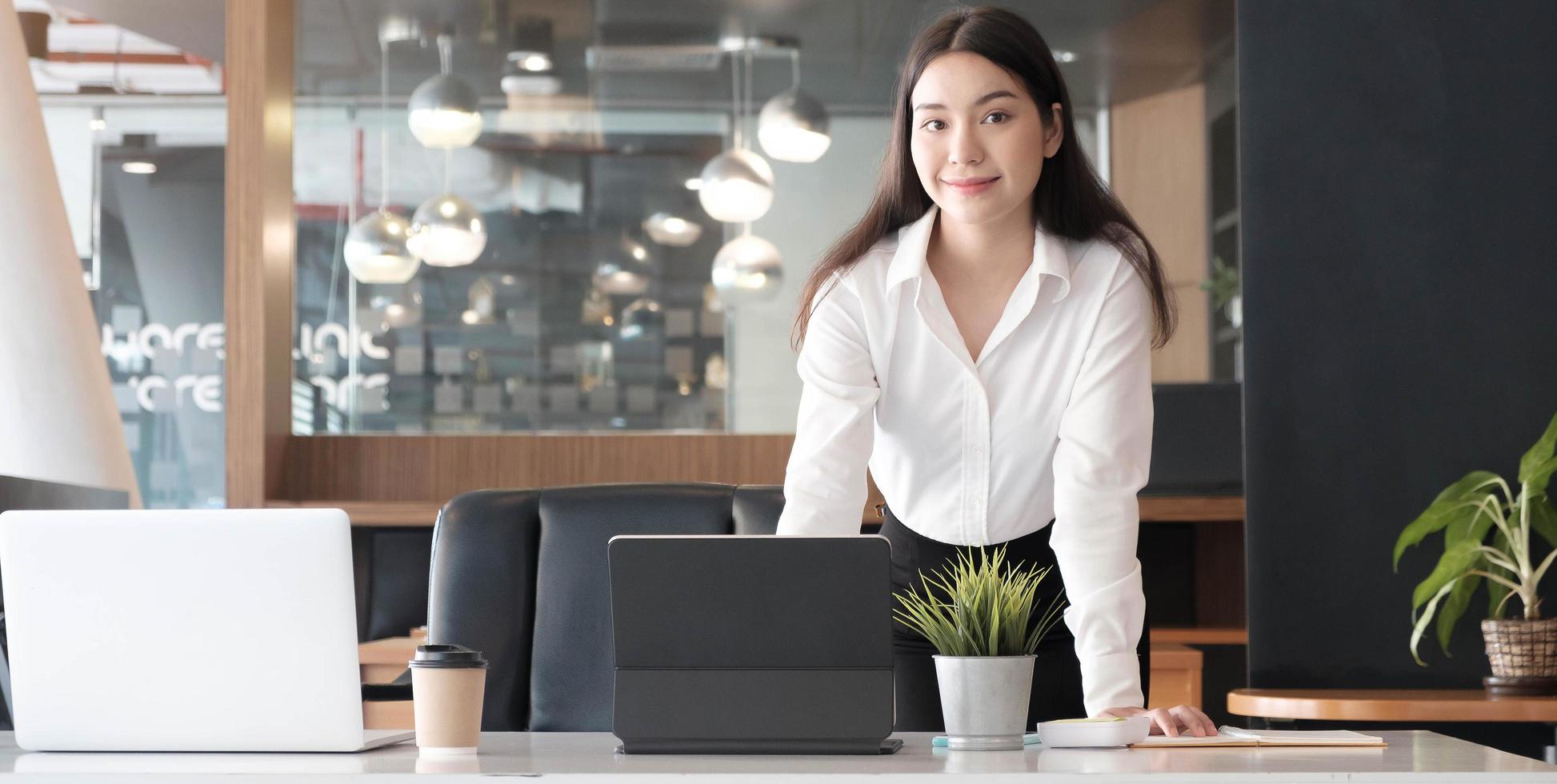 femme d'affaires confiante debout à son bureau et souriant à la caméra. photo