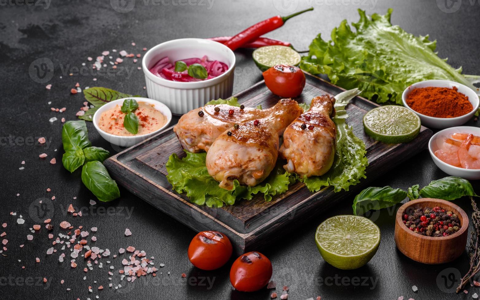 cuisses de poulet grillées savoureuses avec des épices et des herbes sur une planche de bois sur fond de béton foncé photo
