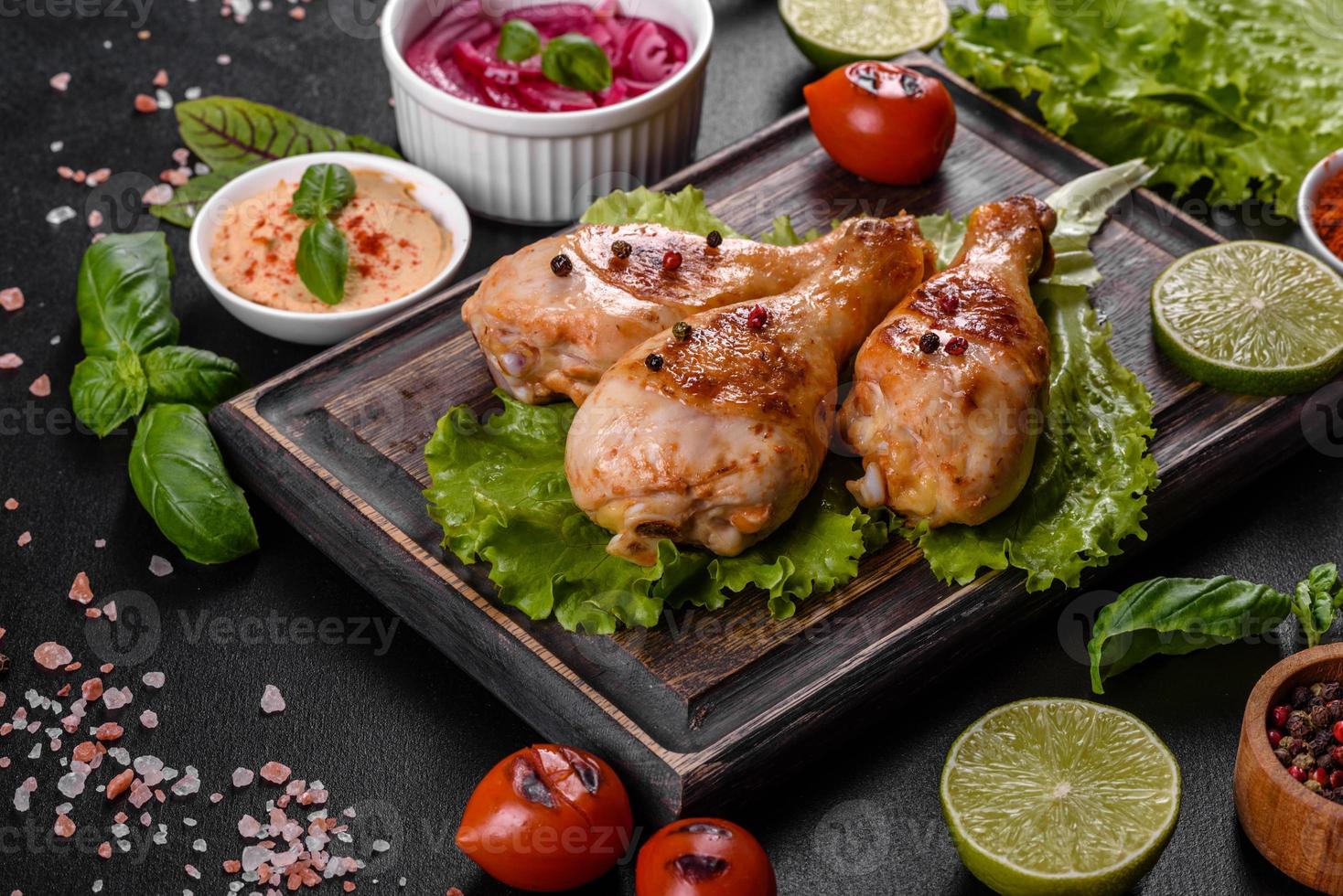 cuisses de poulet grillées savoureuses avec des épices et des herbes sur une planche de bois sur fond de béton foncé photo