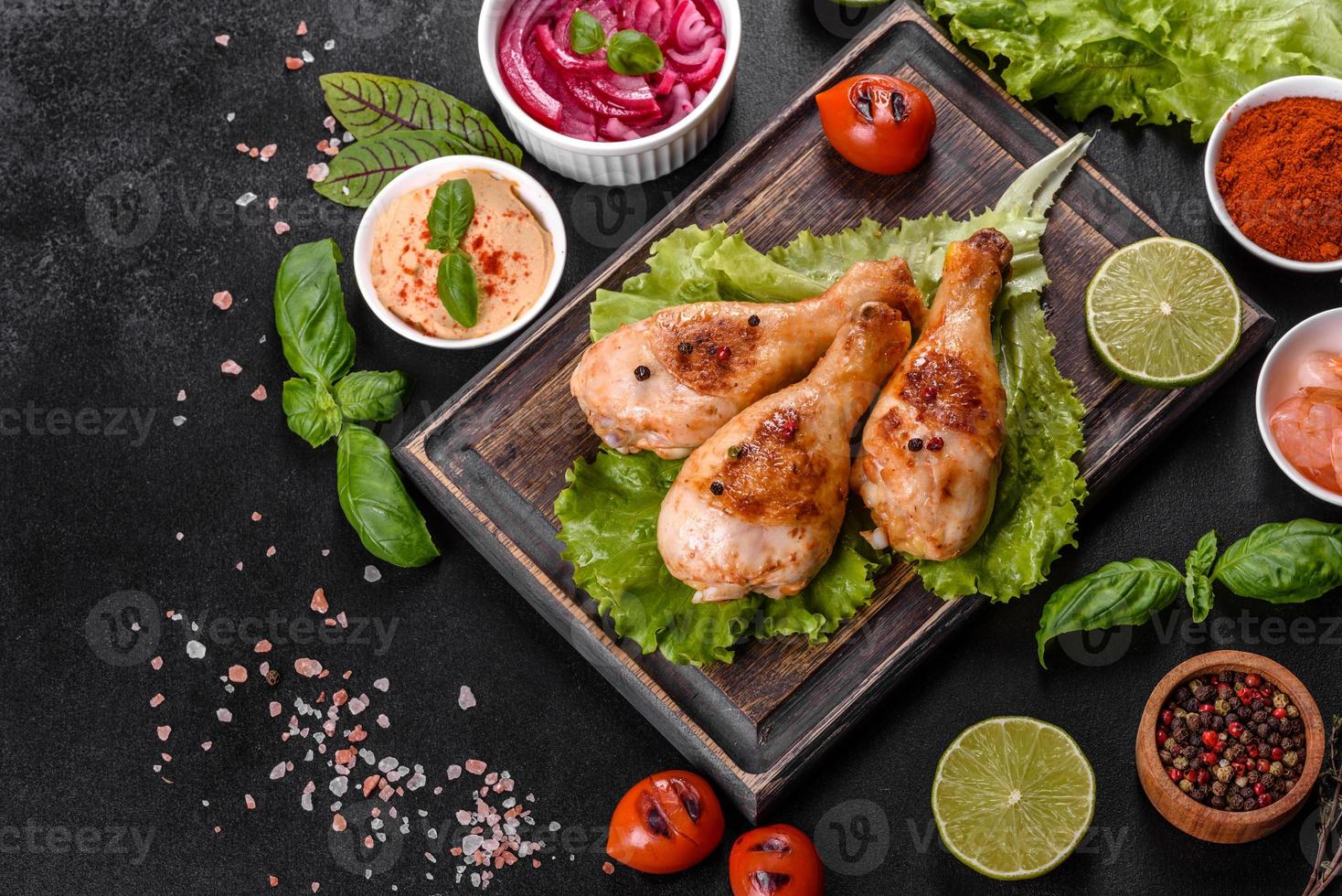 cuisses de poulet grillées savoureuses avec des épices et des herbes sur une planche de bois sur fond de béton foncé photo