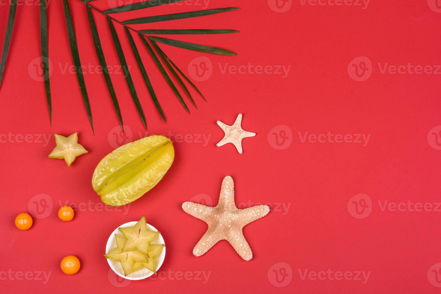 Carambole aux fruits, accessoires de plage et feuillage d'une plante tropicale sur papier de couleur photo