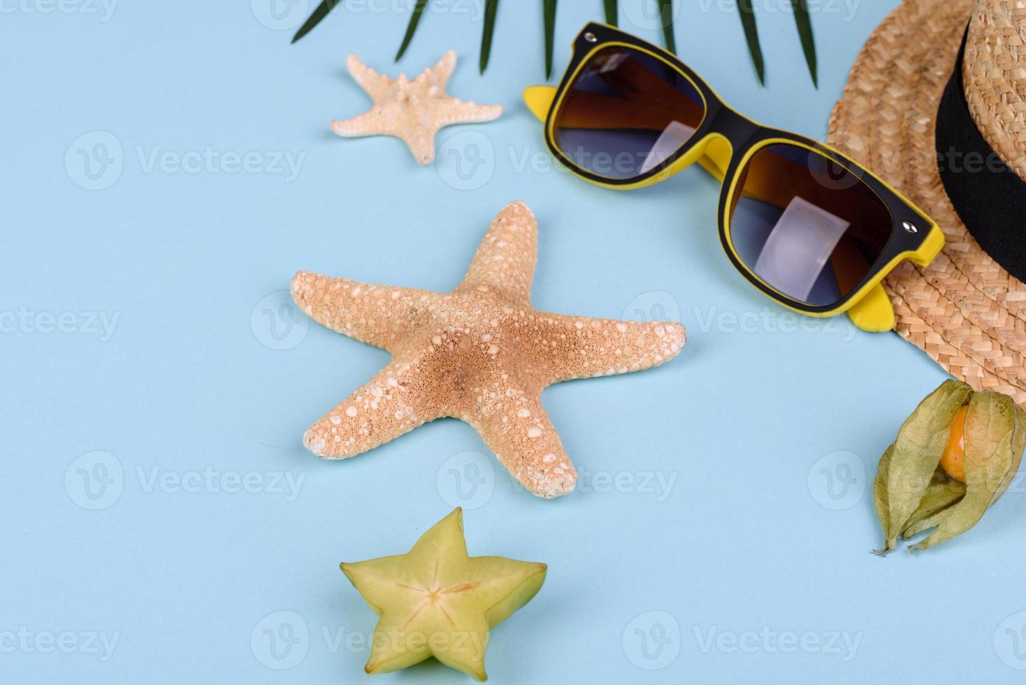Carambole aux fruits, accessoires de plage et feuillage d'une plante tropicale sur papier de couleur photo