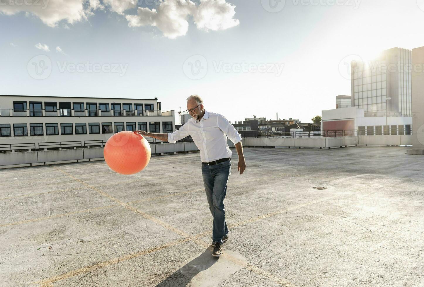 mature homme en jouant avec Orange aptitude Balle sur toit de une gratte-ciel bâtiment photo