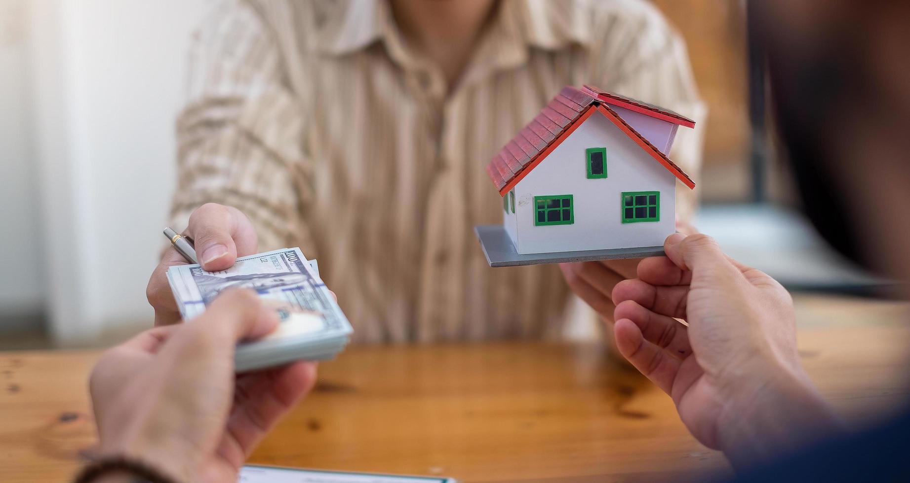 personne remettant des dollars avec un modèle de maison décorative photo