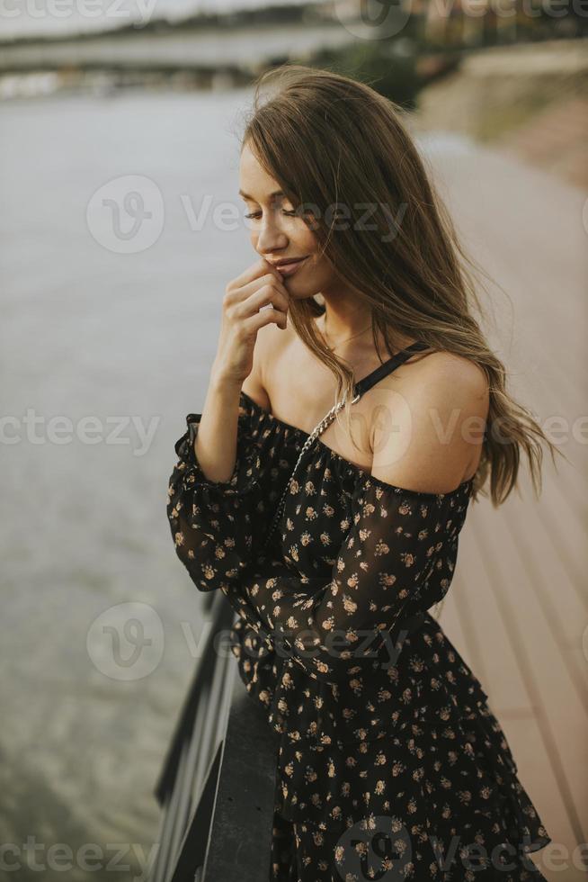 Jeune femme brune aux cheveux longs debout au bord de la rivière photo