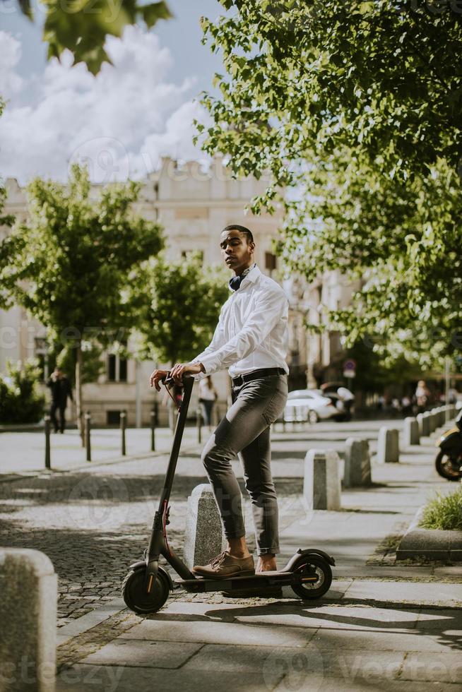 Jeune afro-américain à l'aide d'un scooter électrique dans une rue photo