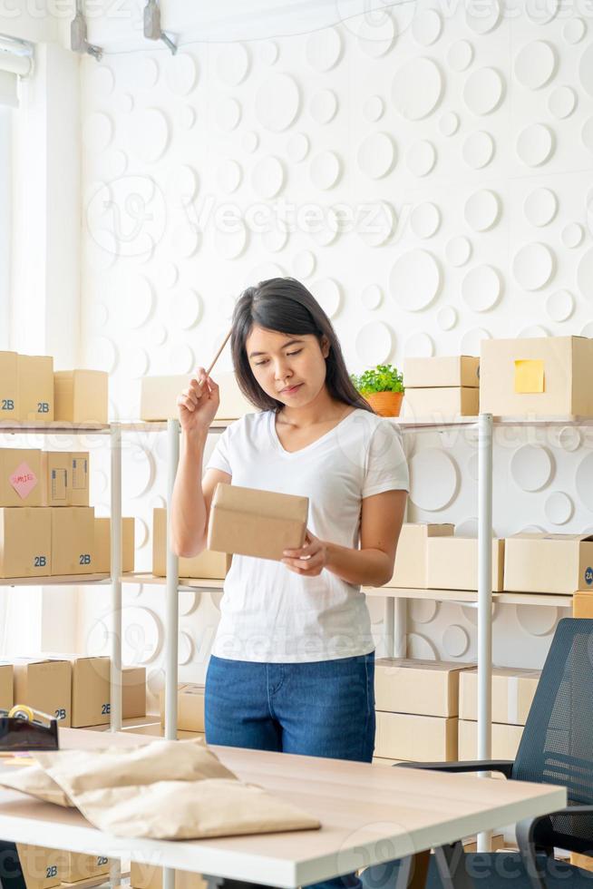 femme asiatique propriétaire d'entreprise travaillant à la maison avec une boîte d'emballage sur le lieu de travail - achat en ligne PME entrepreneur ou concept de travail indépendant photo