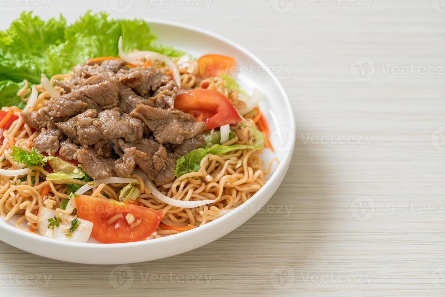Salade épicée de nouilles instantanées avec du porc sur une assiette blanche - style cuisine asiatique photo