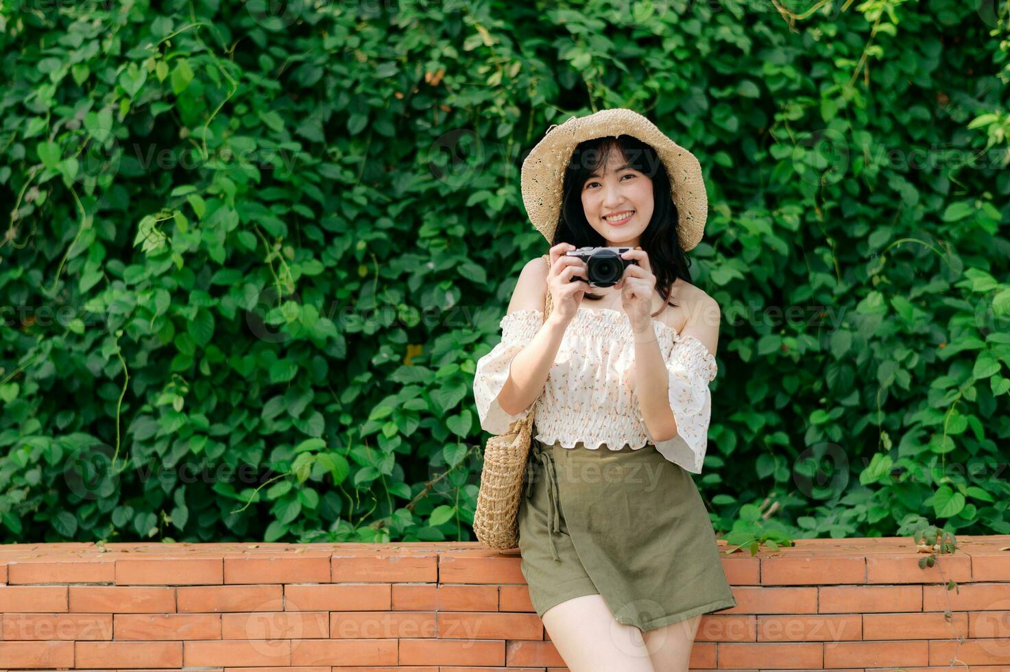 portrait de asiatique Jeune femme voyageur avec tissage chapeau et panier et une caméra sur vert Publique parc la nature Contexte. périple voyage mode de vie, monde Voyage explorateur ou Asie été tourisme concept. photo