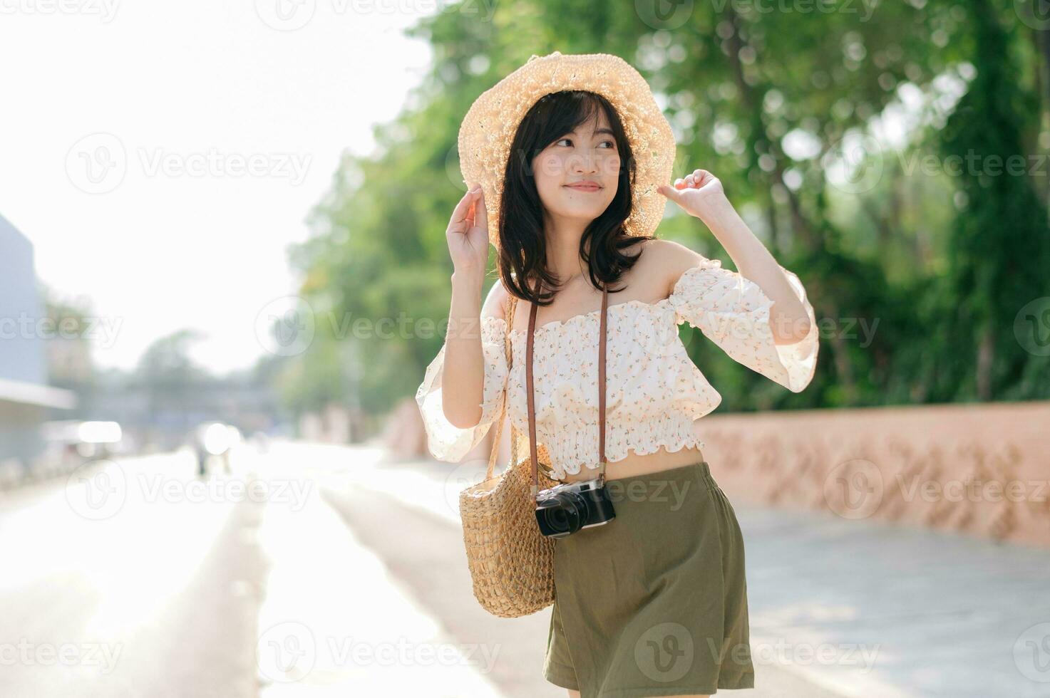 portrait de asiatique Jeune femme voyageur avec tissage chapeau et panier et une caméra sur vert Publique parc la nature Contexte. périple voyage mode de vie, monde Voyage explorateur ou Asie été tourisme concept. photo