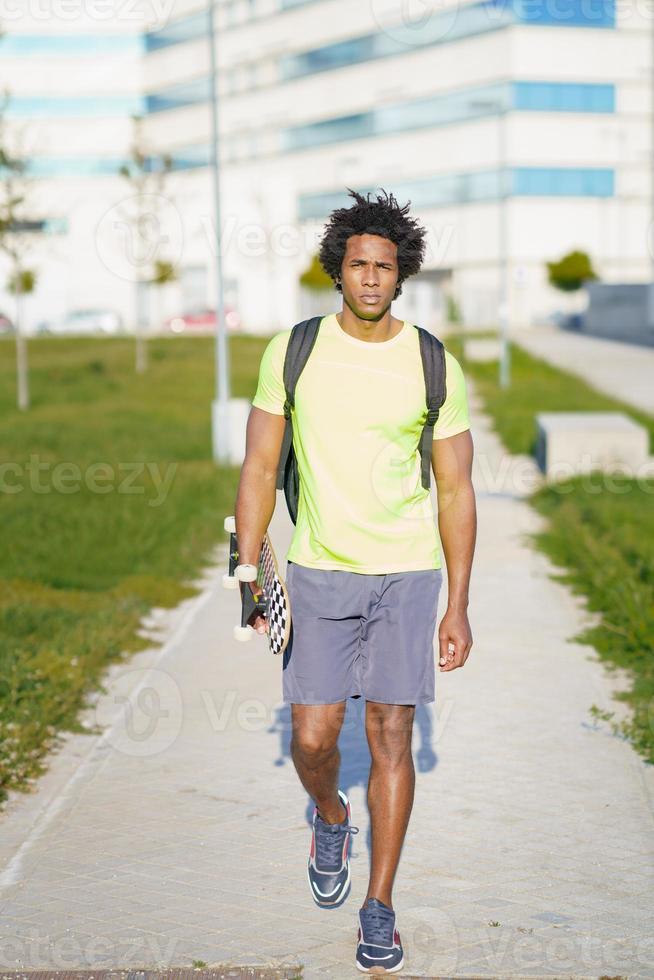 homme noir va pour une séance d'entraînement en vêtements de sport et une planche à roulettes. photo