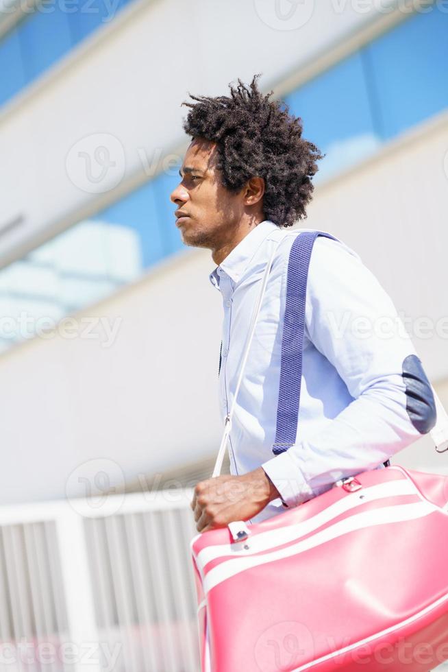 travailleur noir marchant près d'un immeuble de bureaux avec un sac de sport. photo