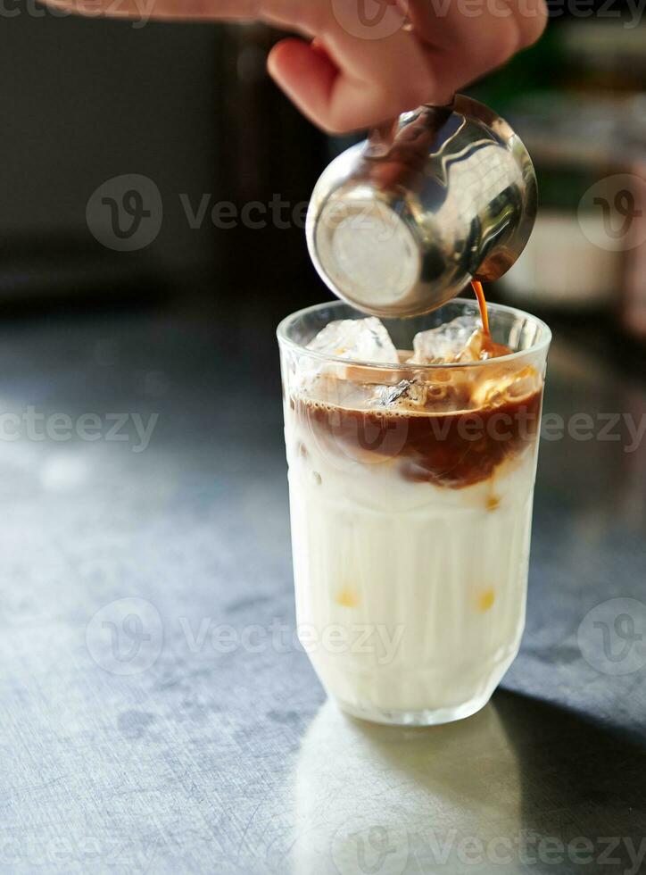 fermer de barista main verser café dans une verre avec fouetté Lait avec la glace tandis que en train de préparer un la glace latté café photo