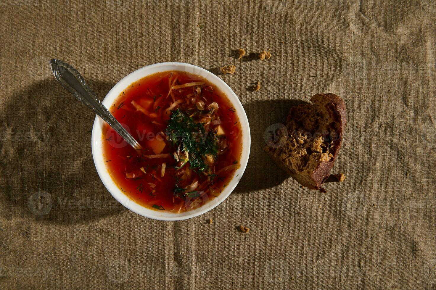 aérien vue de le Bortsch, ukrainien traditionnel soupe avec en bonne santé des légumes et tomates, entier grain pain et les miettes sur une lin nappe de table photo