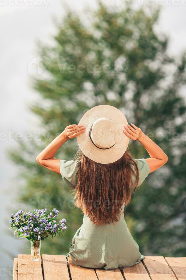 retour vue de Jeune femme asseoir sur une terrasse à une la taille dans le montagnes contre le toile de fond de brouillard et montagnes photo