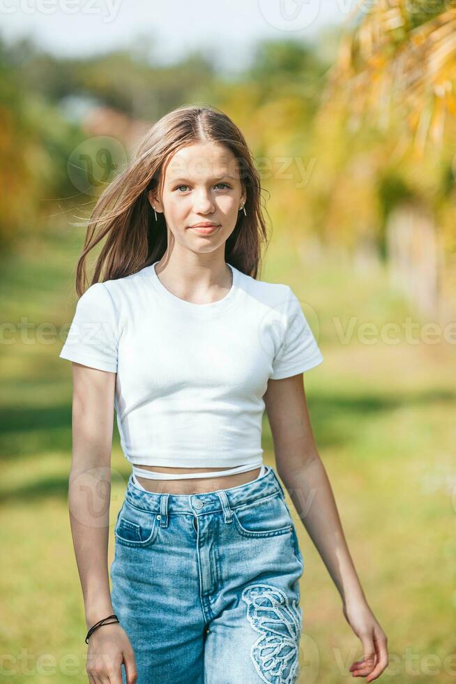 une fille dans une blanc chemise et bleu jeans permanent suivant à une paume arbre photo