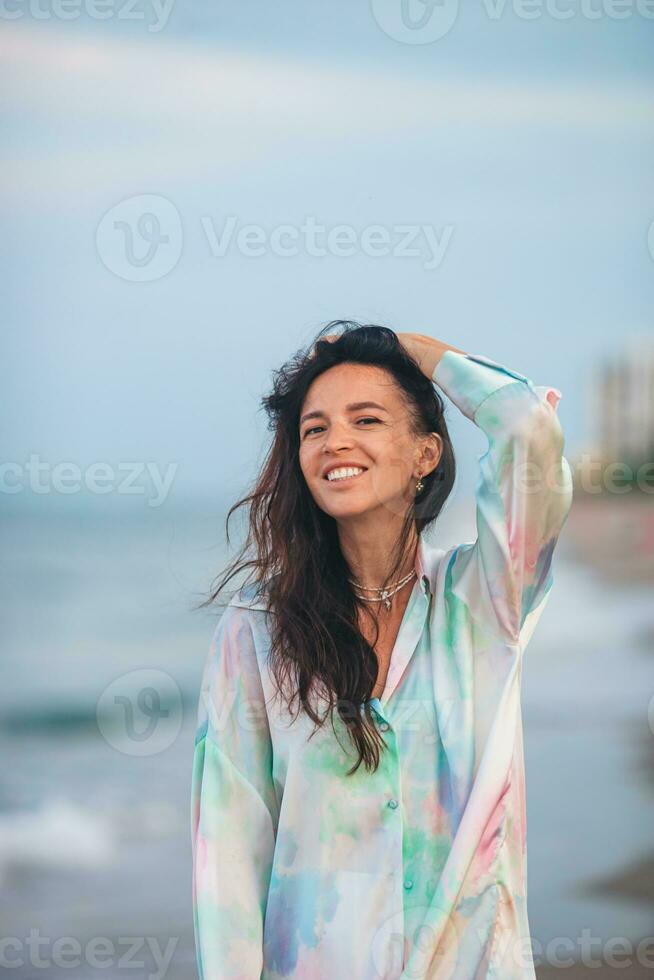 Jeune content femme sur le plage prendre plaisir sa été vacances. femme en marchant le long de le mer dans soir. photo