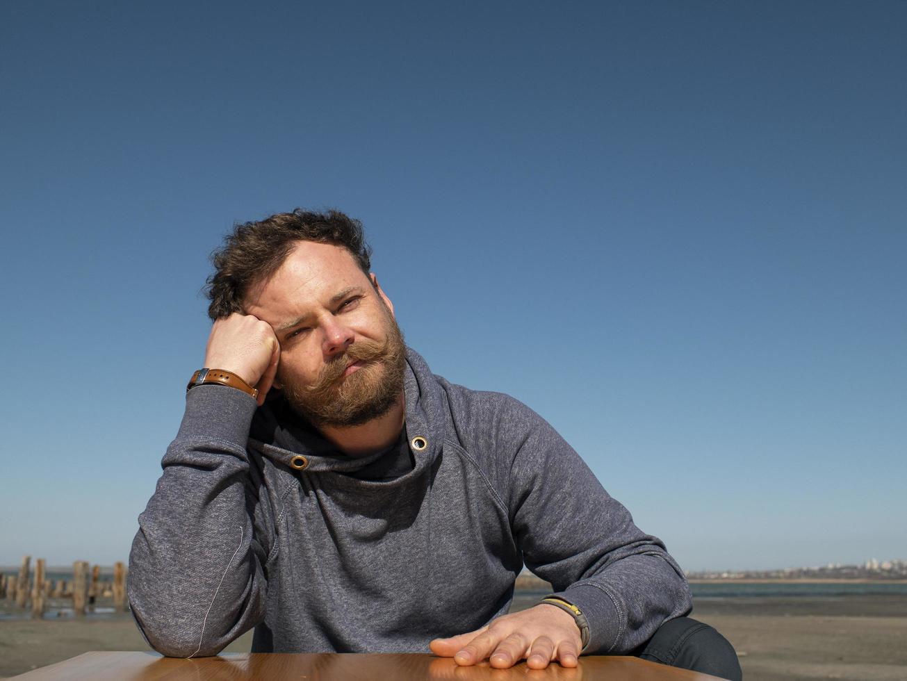 homme pensif avec une barbe assis à une table basse contre un ciel bleu photo