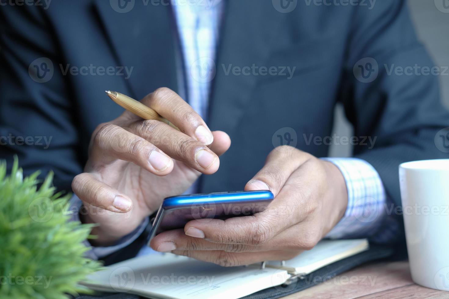 main de jeune homme utilisant un téléphone intelligent et écrivant sur le bloc-notes au bureau photo
