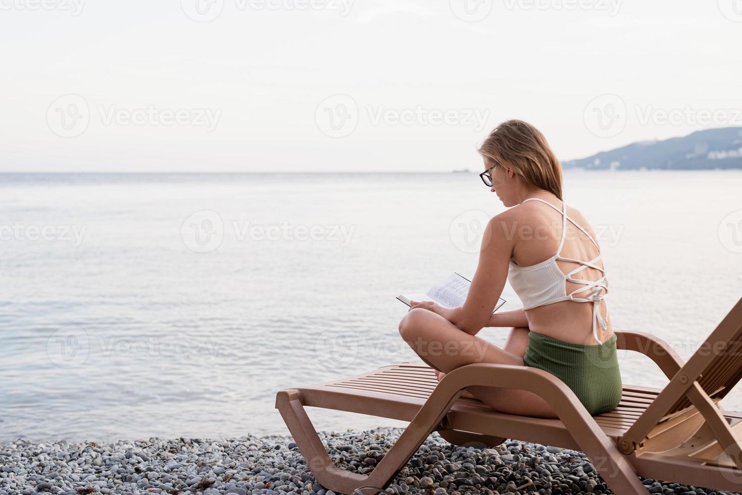 la belle jeune femme assise sur la chaise longue en lisant un livre photo