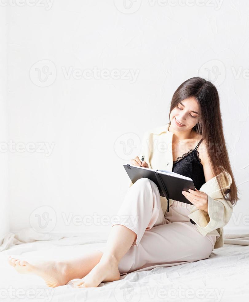 femme dans des vêtements confortables à la maison écrivant des notes assis sur le sol photo